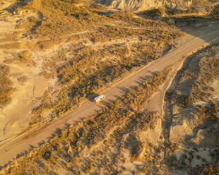 Luftaufnahme eines orangefarbenen Oldtimer-Wohnmobils in der Wüste Bardenas Reales bei Sonnenaufgang, Navarra, Spanien. - AAEF24831