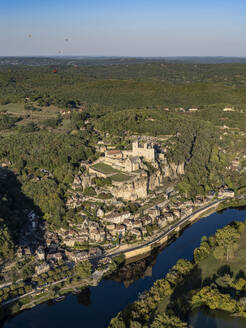 Luftaufnahme des Dorfes La Roque-Gageac und der Burg auf dem Hügel entlang der Dordogne mit Heißluftballons am Himmel, Nouvelle-Aquitaine, Südwestfrankreich - AAEF25038