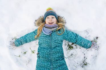 Glückliches Mädchen liegt auf dem Rücken und macht Schneeengel - IHF01848