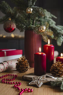 Rote Kerzen neben getöpfertem Weihnachtsbaum mit Dekoration auf dem Tisch - ALKF00913