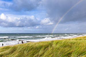 Deutschland, Mecklenburg-Vorpommern, Grasbewachsener Strand mit Regenbogen vor wolkenverhangenem Himmel über dem Meer im Hintergrund - EGBF00995