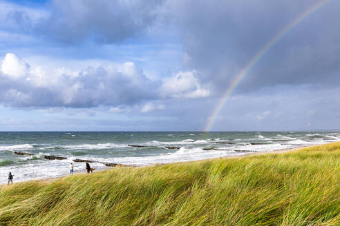 Germany, Mecklenburg-Vorpommern, Grassy beach with rainbow arching against cloudy sky over sea in background - EGBF00995
