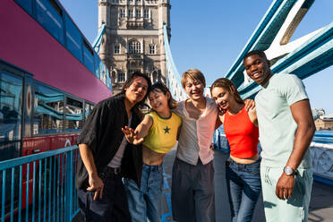 Multirassische Gruppe von glücklichen jungen Freunden in der Londoner City - Multiethnische Teenager treffen sich und haben Spaß in der Tower Bridge, UK - Konzepte über jugendlichen Lebensstil, Reisen und Tourismus - DMDF08362
