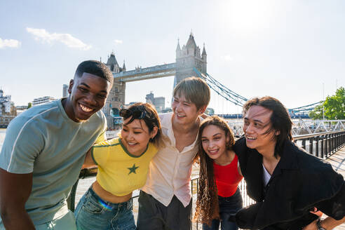 Multirassische Gruppe von glücklichen jungen Freunden in der Londoner City - Multiethnische Teenager treffen sich und haben Spaß in der Tower Bridge, UK - Konzepte über jugendlichen Lebensstil, Reisen und Tourismus - DMDF08365