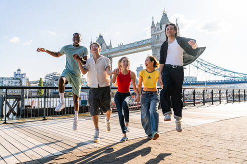 Multirassische Gruppe von glücklichen jungen Freunden in der Londoner City - Multiethnische Teenager treffen sich und haben Spaß in der Tower Bridge, UK - Konzepte über jugendlichen Lebensstil, Reisen und Tourismus - DMDF08373
