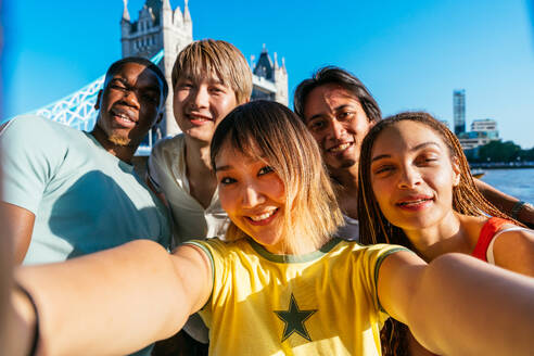 Multirassische Gruppe von glücklichen jungen Freunden in der Londoner City - Multiethnische Teenager treffen sich und haben Spaß in der Tower Bridge, UK - Konzepte über jugendlichen Lebensstil, Reisen und Tourismus - DMDF08381