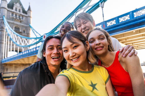 Multirassische Gruppe von glücklichen jungen Freunden in der Londoner City - Multiethnische Teenager treffen sich und haben Spaß in der Tower Bridge, UK - Konzepte über jugendlichen Lebensstil, Reisen und Tourismus - DMDF08388