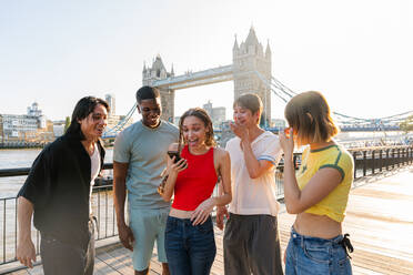 Multirassische Gruppe von glücklichen jungen Freunden in der Londoner City - Multiethnische Teenager treffen sich und haben Spaß in der Tower Bridge, UK - Konzepte über jugendlichen Lebensstil, Reisen und Tourismus - DMDF08390