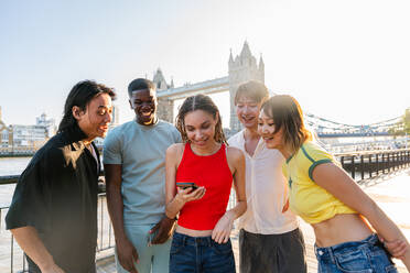 Multirassische Gruppe von glücklichen jungen Freunden in der Londoner City - Multiethnische Teenager treffen sich und haben Spaß in der Tower Bridge, UK - Konzepte über jugendlichen Lebensstil, Reisen und Tourismus - DMDF08391