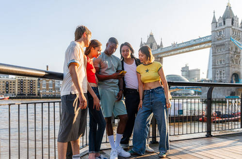 Multirassische Gruppe von glücklichen jungen Freunden in der Londoner City - Multiethnische Teenager treffen sich und haben Spaß in der Tower Bridge, UK - Konzepte über jugendlichen Lebensstil, Reisen und Tourismus - DMDF08395