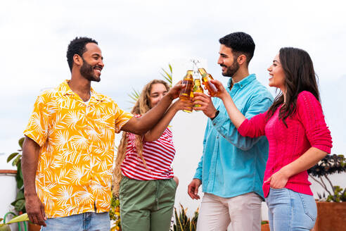 Multiethnische Gruppe von glücklichen jungen Freunden mit Abendessen Grillparty auf dem Dach zu Hause - Multirassische fröhliche junge erwachsene Menschen, die Spaß haben und sich auf einer Terrasse Balkon mit Blick auf die Stadt, Essen und Trinken. - DMDF08532