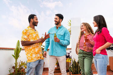 Multiethnische Gruppe von glücklichen jungen Freunden mit Abendessen Grillparty auf dem Dach zu Hause - Multirassische fröhliche junge erwachsene Menschen, die Spaß haben und sich auf einer Terrasse Balkon mit Blick auf die Stadt, Essen und Trinken. - DMDF08535