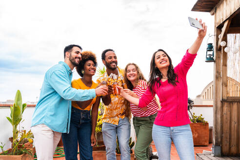 Multiethnische Gruppe von glücklichen jungen Freunden mit Abendessen Grillparty auf dem Dach zu Hause - Multirassische fröhliche junge erwachsene Menschen, die Spaß haben und sich auf einer Terrasse Balkon mit Blick auf die Stadt, Essen und Trinken. - DMDF08545
