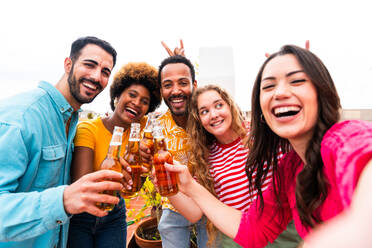 Multiethnische Gruppe von glücklichen jungen Freunden mit Abendessen Grillparty auf dem Dach zu Hause - Multirassische fröhliche junge erwachsene Menschen, die Spaß haben und sich auf einer Terrasse Balkon mit Blick auf die Stadt, Essen und Trinken. - DMDF08550