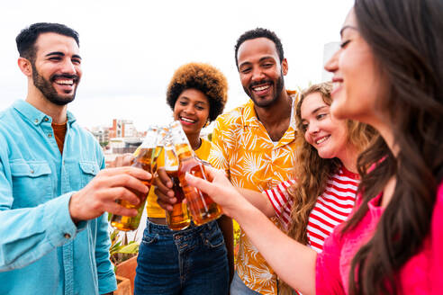 Multiethnische Gruppe von glücklichen jungen Freunden mit Abendessen Grillparty auf dem Dach zu Hause - Multirassische fröhliche junge erwachsene Menschen, die Spaß haben und sich auf einer Terrasse Balkon mit Blick auf die Stadt, Essen und Trinken. - DMDF08554