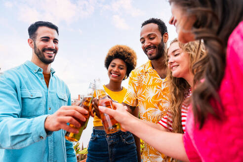 Multiethnische Gruppe von glücklichen jungen Freunden mit Abendessen Grillparty auf dem Dach zu Hause - Multirassische fröhliche junge erwachsene Menschen, die Spaß haben und sich auf einer Terrasse Balkon mit Blick auf die Stadt, Essen und Trinken. - DMDF08555