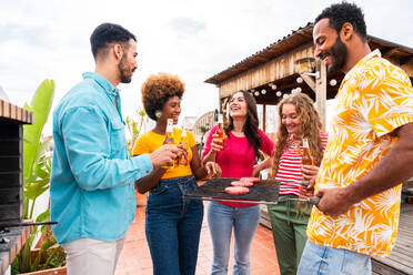 Multiethnische Gruppe von glücklichen jungen Freunden mit Abendessen Grillparty auf dem Dach zu Hause - Multirassische fröhliche junge erwachsene Menschen, die Spaß haben und sich auf einer Terrasse Balkon mit Blick auf die Stadt, Essen und Trinken. - DMDF08558