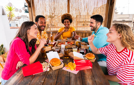 Multiethnische Gruppe von glücklichen jungen Freunden mit Abendessen Grillparty auf dem Dach zu Hause - Multirassische fröhliche junge erwachsene Menschen, die Spaß haben und sich auf einer Terrasse Balkon mit Blick auf die Stadt, Essen und Trinken. - DMDF08571