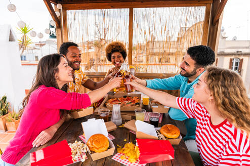 Multiethnische Gruppe von glücklichen jungen Freunden mit Abendessen Grillparty auf dem Dach zu Hause - Multirassische fröhliche junge erwachsene Menschen, die Spaß haben und sich auf einer Terrasse Balkon mit Blick auf die Stadt, Essen und Trinken. - DMDF08572