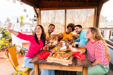 Multiethnische Gruppe von glücklichen jungen Freunden mit Abendessen Grillparty auf dem Dach zu Hause - Multirassische fröhliche junge erwachsene Menschen, die Spaß haben und sich auf einer Terrasse Balkon mit Blick auf die Stadt, Essen und Trinken. - DMDF08576