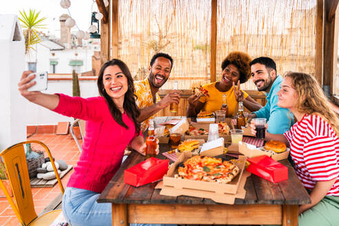 Multiethnische Gruppe von glücklichen jungen Freunden mit Abendessen Grillparty auf dem Dach zu Hause - Multirassische fröhliche junge erwachsene Menschen, die Spaß haben und sich auf einer Terrasse Balkon mit Blick auf die Stadt, Essen und Trinken. - DMDF08577