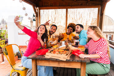 Multiethnische Gruppe von glücklichen jungen Freunden mit Abendessen Grillparty auf dem Dach zu Hause - Multirassische fröhliche junge erwachsene Menschen, die Spaß haben und sich auf einer Terrasse Balkon mit Blick auf die Stadt, Essen und Trinken. - DMDF08579