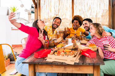 Multiethnische Gruppe von glücklichen jungen Freunden mit Abendessen Grillparty auf dem Dach zu Hause - Multirassische fröhliche junge erwachsene Menschen, die Spaß haben und sich auf einer Terrasse Balkon mit Blick auf die Stadt, Essen und Trinken. - DMDF08580