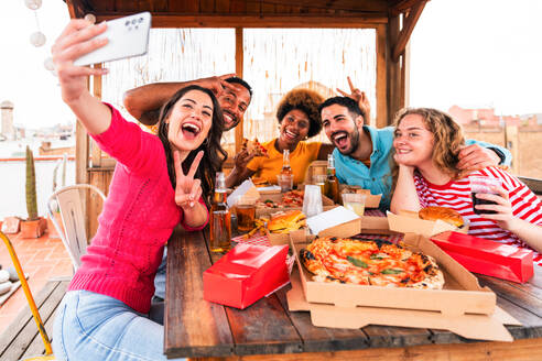 Multiethnische Gruppe von glücklichen jungen Freunden mit Abendessen Grillparty auf dem Dach zu Hause - Multirassische fröhliche junge erwachsene Menschen, die Spaß haben und sich auf einer Terrasse Balkon mit Blick auf die Stadt, Essen und Trinken. - DMDF08581