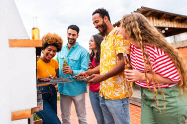Multiethnische Gruppe von glücklichen jungen Freunden mit Abendessen Grillparty auf dem Dach zu Hause - Multirassische fröhliche junge erwachsene Menschen, die Spaß haben und sich auf einer Terrasse Balkon mit Blick auf die Stadt, Essen und Trinken. - DMDF08591