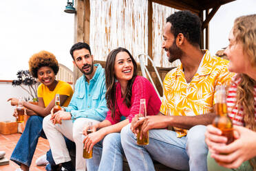 Multiethnische Gruppe von glücklichen jungen Freunden mit Abendessen Grillparty auf dem Dach zu Hause - Multirassische fröhliche junge erwachsene Menschen, die Spaß haben und sich auf einer Terrasse Balkon mit Blick auf die Stadt, Essen und Trinken. - DMDF08596