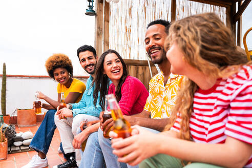 Multiethnische Gruppe von glücklichen jungen Freunden mit Abendessen Grillparty auf dem Dach zu Hause - Multirassische fröhliche junge erwachsene Menschen, die Spaß haben und sich auf einer Terrasse Balkon mit Blick auf die Stadt, Essen und Trinken. - DMDF08597