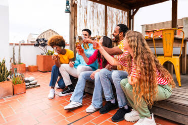 Multiethnische Gruppe von glücklichen jungen Freunden mit Abendessen Grillparty auf dem Dach zu Hause - Multirassische fröhliche junge erwachsene Menschen, die Spaß haben und sich auf einer Terrasse Balkon mit Blick auf die Stadt, Essen und Trinken. - DMDF08600