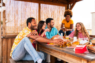 Multiethnische Gruppe von glücklichen jungen Freunden mit Abendessen Grillparty auf dem Dach zu Hause - Multirassische fröhliche junge erwachsene Menschen, die Spaß haben und sich auf einer Terrasse Balkon mit Blick auf die Stadt, Essen und Trinken. - DMDF08603