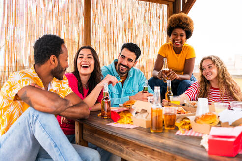 Multiethnische Gruppe von glücklichen jungen Freunden mit Abendessen Grillparty auf dem Dach zu Hause - Multirassische fröhliche junge erwachsene Menschen, die Spaß haben und sich auf einer Terrasse Balkon mit Blick auf die Stadt, Essen und Trinken. - DMDF08605