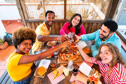 Multiethnische Gruppe von glücklichen jungen Freunden mit Abendessen Grillparty auf dem Dach zu Hause - Multirassische fröhliche junge erwachsene Menschen, die Spaß haben und sich auf einer Terrasse Balkon mit Blick auf die Stadt, Essen und Trinken. - DMDF08611