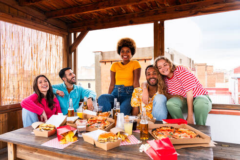 Multiethnische Gruppe von glücklichen jungen Freunden mit Abendessen Grillparty auf dem Dach zu Hause - Multirassische fröhliche junge erwachsene Menschen, die Spaß haben und sich auf einer Terrasse Balkon mit Blick auf die Stadt, Essen und Trinken. - DMDF08613