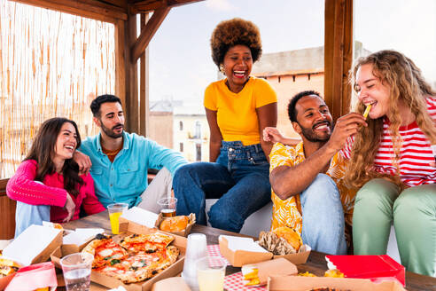 Multiethnische Gruppe von glücklichen jungen Freunden mit Abendessen Grillparty auf dem Dach zu Hause - Multirassische fröhliche junge erwachsene Menschen, die Spaß haben und sich auf einer Terrasse Balkon mit Blick auf die Stadt, Essen und Trinken. - DMDF08615