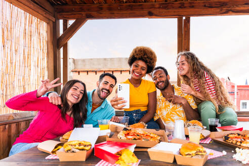 Multiethnische Gruppe von glücklichen jungen Freunden mit Abendessen Grillparty auf dem Dach zu Hause - Multirassische fröhliche junge erwachsene Menschen, die Spaß haben und sich auf einer Terrasse Balkon mit Blick auf die Stadt, Essen und Trinken. - DMDF08616