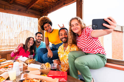 Multiethnische Gruppe von glücklichen jungen Freunden mit Abendessen Grillparty auf dem Dach zu Hause - Multirassische fröhliche junge erwachsene Menschen, die Spaß haben und sich auf einer Terrasse Balkon mit Blick auf die Stadt, Essen und Trinken. - DMDF08617