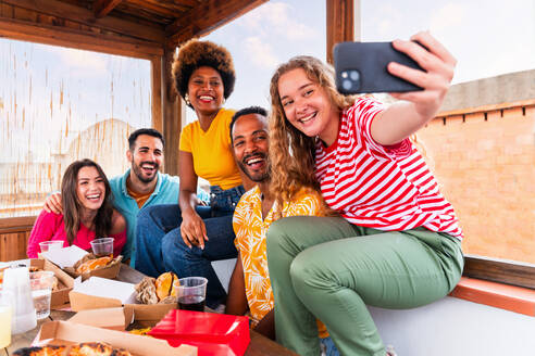 Multiethnische Gruppe von glücklichen jungen Freunden mit Abendessen Grillparty auf dem Dach zu Hause - Multirassische fröhliche junge erwachsene Menschen, die Spaß haben und sich auf einer Terrasse Balkon mit Blick auf die Stadt, Essen und Trinken. - DMDF08618