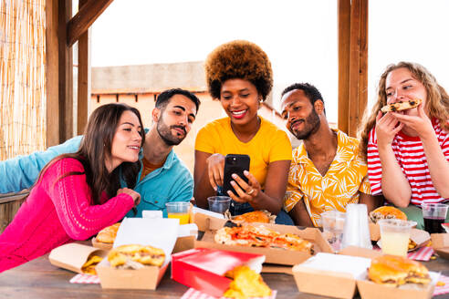 Multiethnische Gruppe von glücklichen jungen Freunden mit Abendessen Grillparty auf dem Dach zu Hause - Multirassische fröhliche junge erwachsene Menschen, die Spaß haben und sich auf einer Terrasse Balkon mit Blick auf die Stadt, Essen und Trinken. - DMDF08619