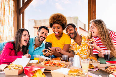 Multiethnische Gruppe von glücklichen jungen Freunden mit Abendessen Grillparty auf dem Dach zu Hause - Multirassische fröhliche junge erwachsene Menschen, die Spaß haben und sich auf einer Terrasse Balkon mit Blick auf die Stadt, Essen und Trinken. - DMDF08620