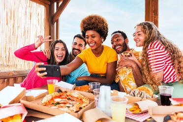 Multiethnische Gruppe von glücklichen jungen Freunden mit Abendessen Grillparty auf dem Dach zu Hause - Multirassische fröhliche junge erwachsene Menschen, die Spaß haben und sich auf einer Terrasse Balkon mit Blick auf die Stadt, Essen und Trinken. - DMDF08622