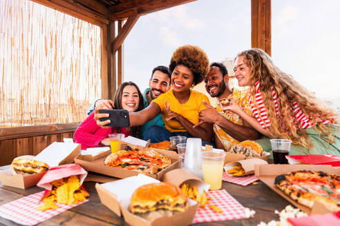 Multiethnische Gruppe von glücklichen jungen Freunden mit Abendessen Grillparty auf dem Dach zu Hause - Multirassische fröhliche junge erwachsene Menschen, die Spaß haben und sich auf einer Terrasse Balkon mit Blick auf die Stadt, Essen und Trinken. - DMDF08623