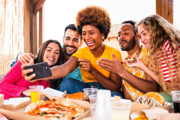 Multiethnische Gruppe von glücklichen jungen Freunden mit Abendessen Grillparty auf dem Dach zu Hause - Multirassische fröhliche junge erwachsene Menschen, die Spaß haben und sich auf einer Terrasse Balkon mit Blick auf die Stadt, Essen und Trinken. - DMDF08624