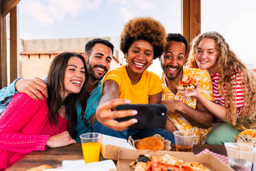 Multiethnische Gruppe von glücklichen jungen Freunden mit Abendessen Grillparty auf dem Dach zu Hause - Multirassische fröhliche junge erwachsene Menschen, die Spaß haben und sich auf einer Terrasse Balkon mit Blick auf die Stadt, Essen und Trinken. - DMDF08625