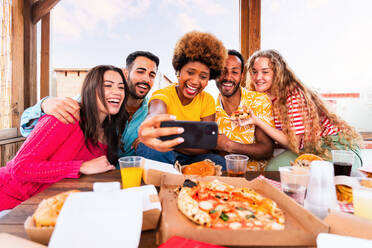 Multiethnische Gruppe von glücklichen jungen Freunden mit Abendessen Grillparty auf dem Dach zu Hause - Multirassische fröhliche junge erwachsene Menschen, die Spaß haben und sich auf einer Terrasse Balkon mit Blick auf die Stadt, Essen und Trinken. - DMDF08626