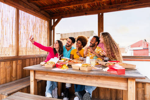 Multiethnische Gruppe von glücklichen jungen Freunden mit Abendessen Grillparty auf dem Dach zu Hause - Multirassische fröhliche junge erwachsene Menschen, die Spaß haben und sich auf einer Terrasse Balkon mit Blick auf die Stadt, Essen und Trinken. - DMDF08627