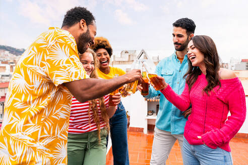 Multiethnische Gruppe von glücklichen jungen Freunden mit Abendessen Grillparty auf dem Dach zu Hause - Multirassische fröhliche junge erwachsene Menschen, die Spaß haben und sich auf einer Terrasse Balkon mit Blick auf die Stadt, Essen und Trinken. - DMDF08629