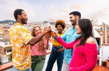 Multiethnische Gruppe von glücklichen jungen Freunden mit Abendessen Grillparty auf dem Dach zu Hause - Multirassische fröhliche junge erwachsene Menschen, die Spaß haben und sich auf einer Terrasse Balkon mit Blick auf die Stadt, Essen und Trinken. - DMDF08630